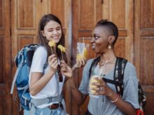 Women Travelers Visiting City with Backpacks Eating Pineapple