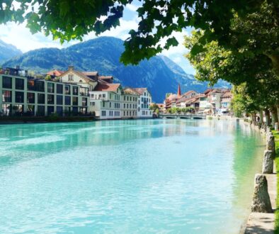 green and white house near green trees and body of water during daytime