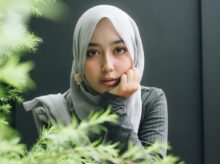 woman wearing gray long-sleeved top and gray hijab right hand on cheek