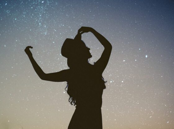 silhouette of woman holding hat in blue and gray nebula