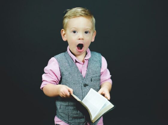 boy wearing gray vest and pink dress shirt holding book