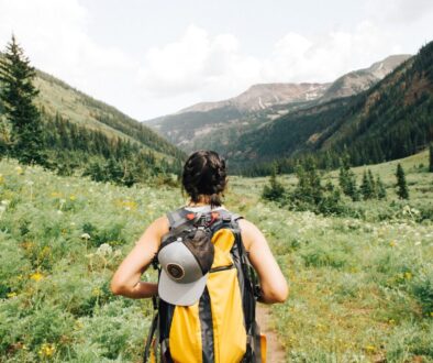 person carrying yellow and black backpack walking between green plants
