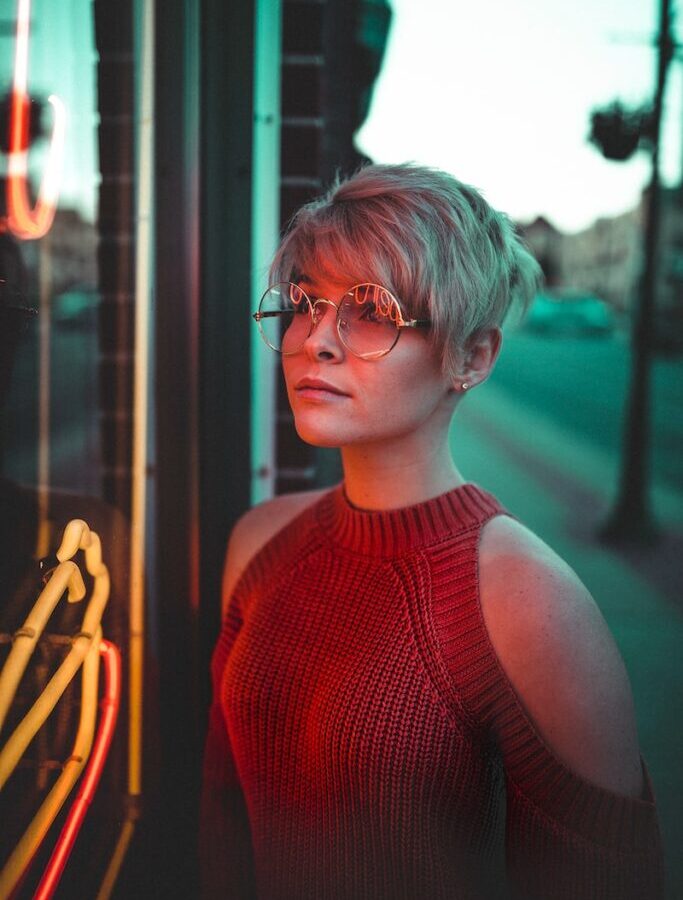 woman with eyeglasses looking at glass panel with neon signage