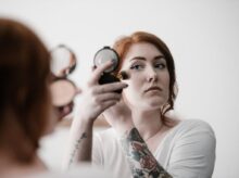 selective focus photography of woman applying blush-on on her face
