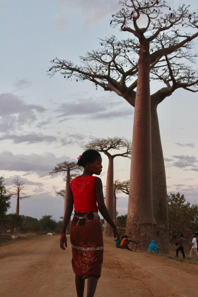 woman in red tank top standing beside brown tree during daytime