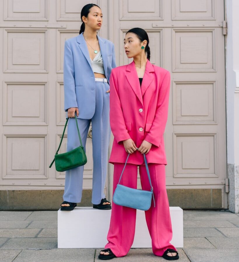 Women in Pink and Blue Blazers Standing on the Street while Holding Bags