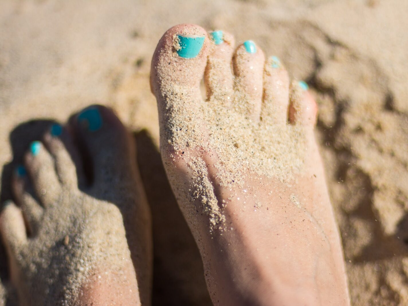 person sky-blue nail polish feet on brown sand