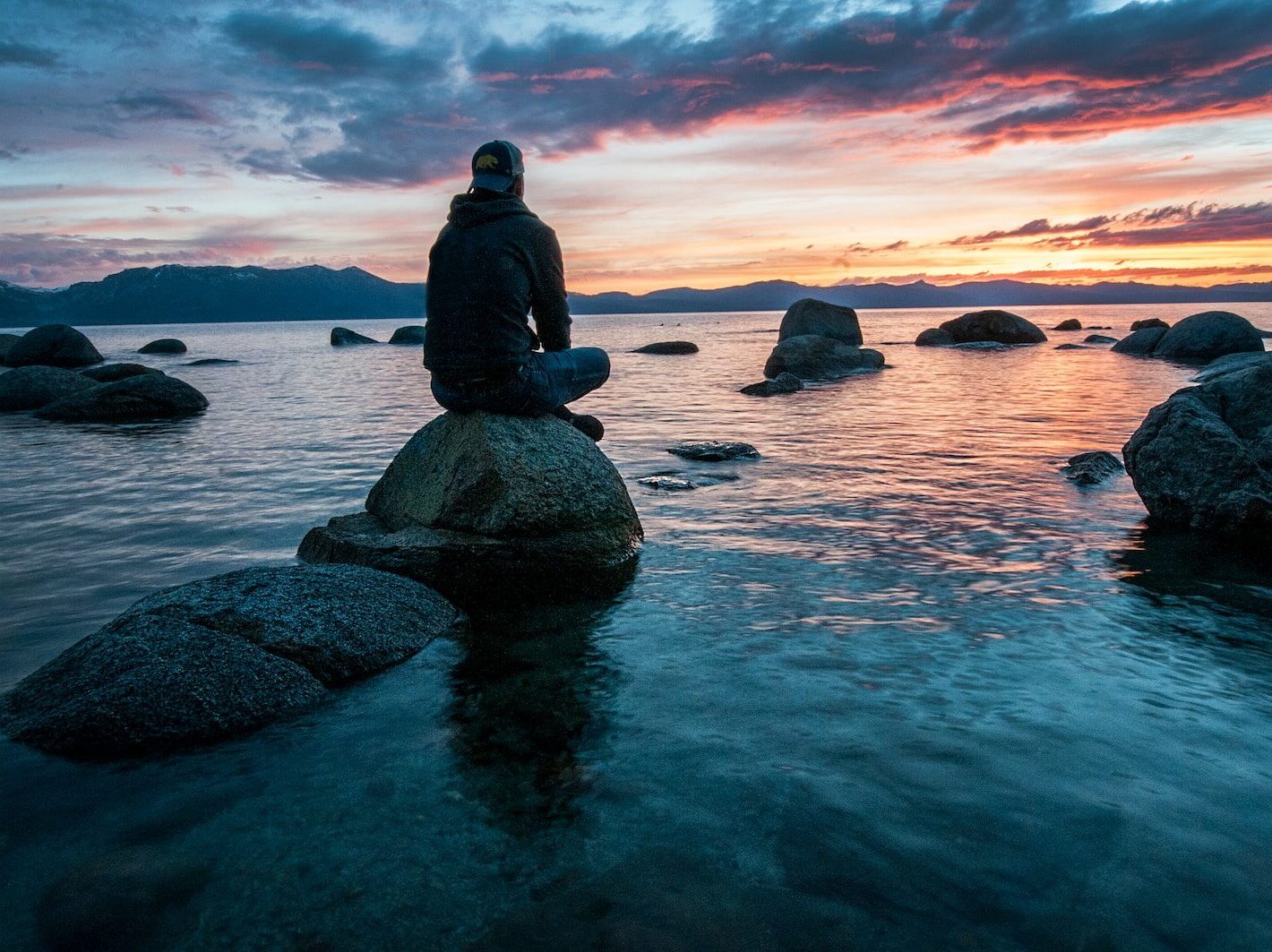 man sitting on rock surrounded by water