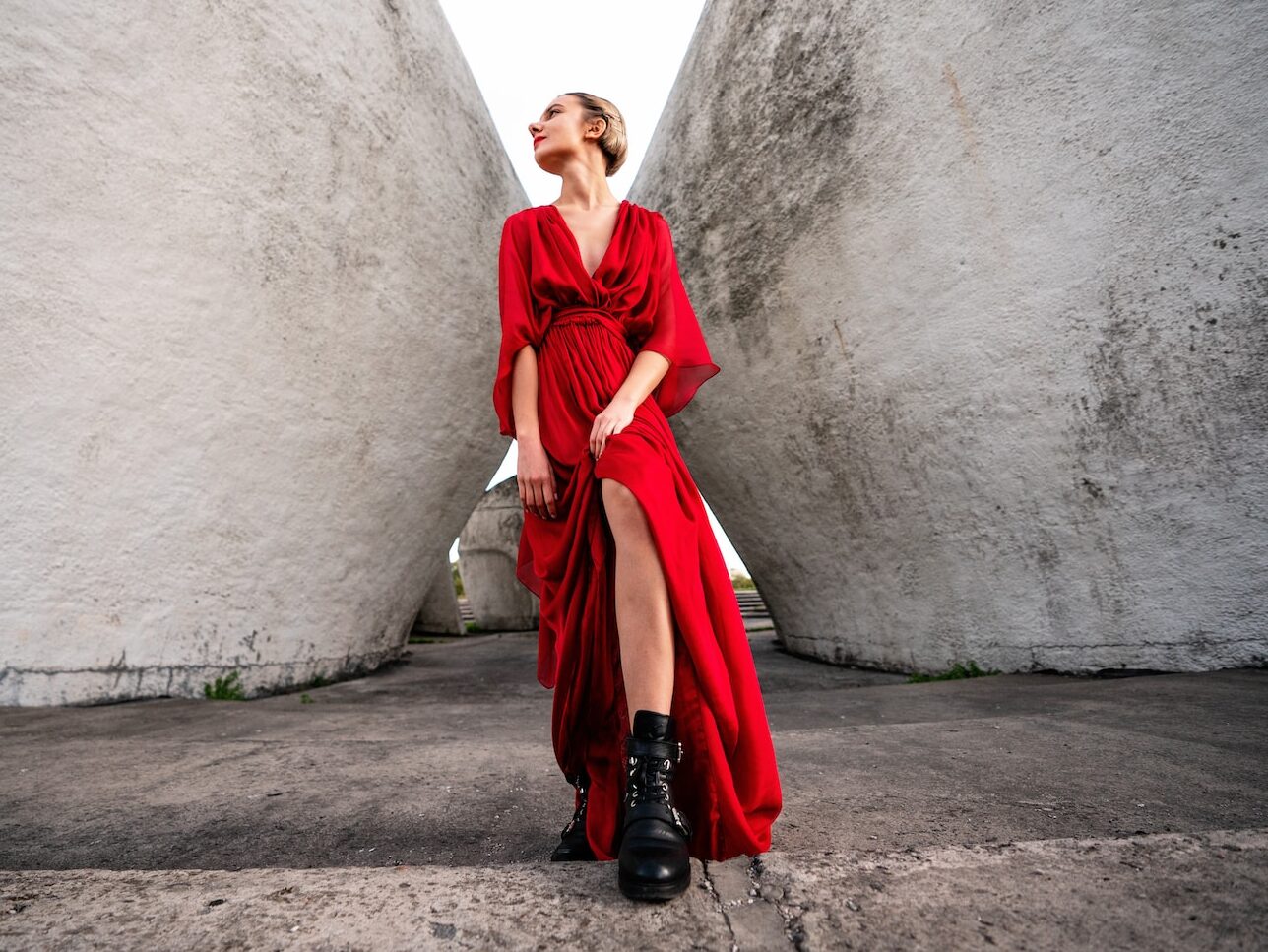 woman in red long sleeve dress and black boots standing beside gray concrete wall during daytime
