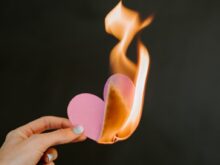 a person holding a paper heart in front of a fire