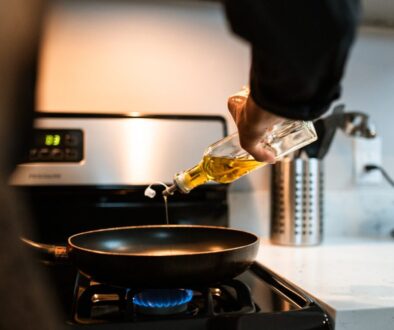 Back view crop unrecognizable person pouring olive or sunflower oil into frying pan placed on stove in domestic kitchen