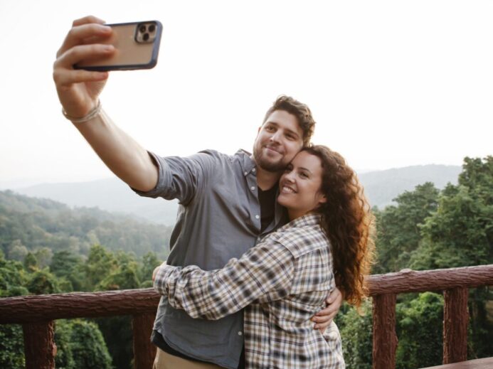 Cheerful young couple hugging while taking selfie on terrace in forest
