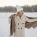 Woman in White Coat with White Knitted Cap Standing on Snow Covered Ground