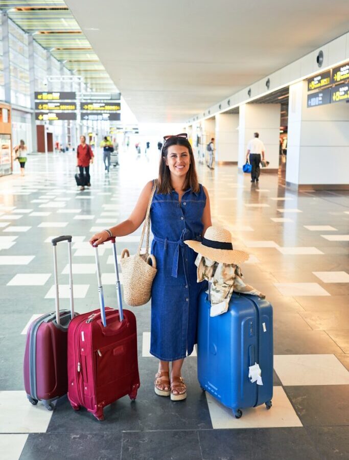 woman in blue denim jacket holding red luggage bag