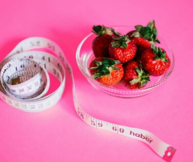 A glass bowl of fresh strawberries paired with a pink measuring tape symbolizes healthy eating.
