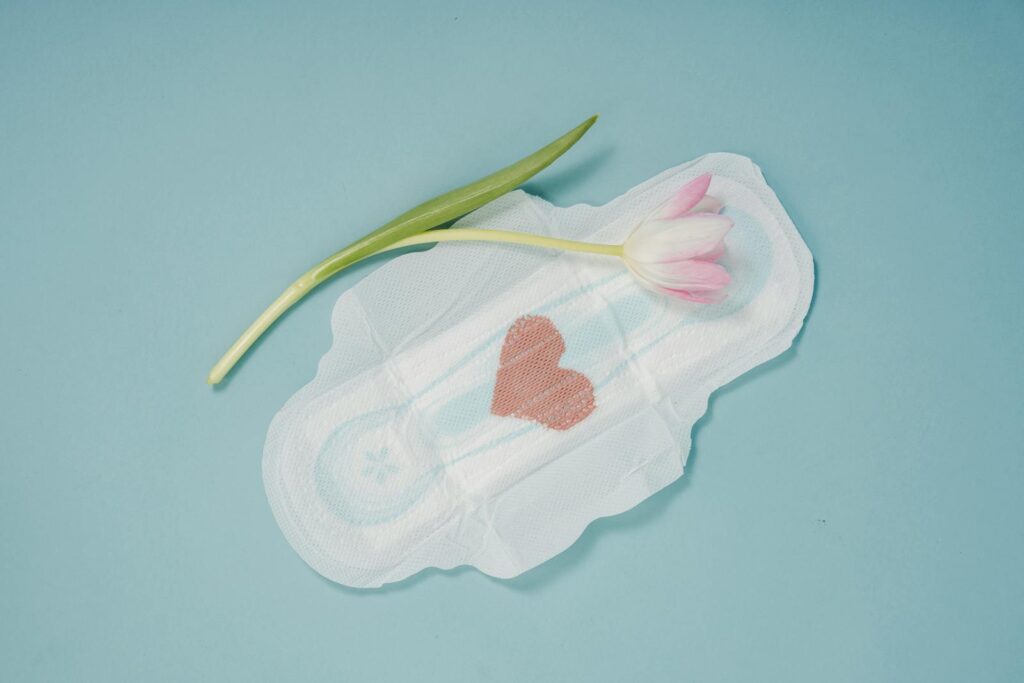A menstrual pad with a pink heart and tulip on a blue surface, symbolizing care and femininity.