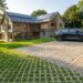 Modern stone-and-wood house with solar panels, green lawn, and a black car parked on a grass-filled paver driveway.