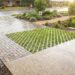 Wet, rain-slick driveway with brick pavers and a triangular grass-grid insert in a xeriscaped front yard.