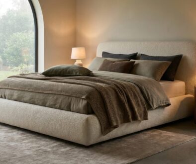 Neutral-toned bedroom with a rounded beige bed, olive and brown bedding, and two bedside lamps by a curved window View outside garden