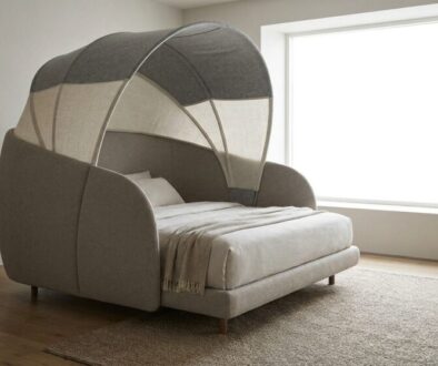 Grey upholstered bed with a curved fabric canopy forming a tent-like canopy in a bright minimalist bedroom.