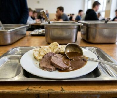 Plate with sliced roast beef, gravy, and bread on a metal cafeteria tray in a busy dining hall.