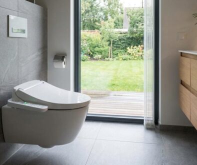 Modern bathroom with a wall-mounted smart toilet and bidet controls, opening to a green garden beyond a glass door.