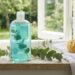 Blue liquid soap bottle with eucalyptus sprigs on a windowsill, sponge and white towel nearby.