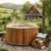 Round wooden hot tub steaming in a garden, with a wood-burning heater and stacked firewood nearby.