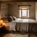 Cozy rustic bedroom with a bed built into a stone alcove, warm lamp on a bench, and a small window with a shade.