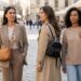 Three women walk and chat on a cobblestone street with outdoor cafes; each carries a bag as they stroll nearby cafes.