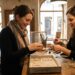 Two women in a craft workshop examining and arranging silver bracelets on a wooden table.