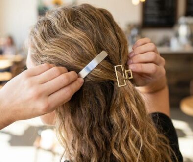 Person styling their wavy blond hair with two metal hair clips in a cafe setting
