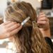 Person styling their wavy blond hair with two metal hair clips in a cafe setting