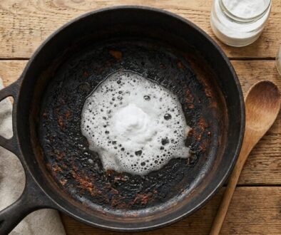 Cast-iron skillet with burnt interior and a foamy white mound in the center, on a rustic wooden table with a towel, salt jar, and a glass bottle nearby.