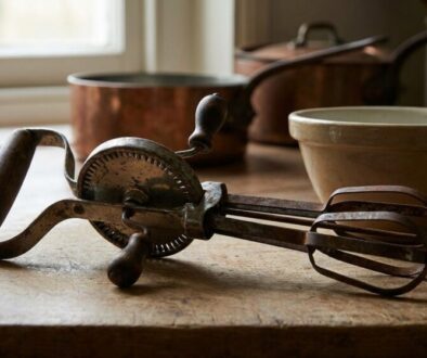 Vintage manual hand mixer with beaters on a wooden kitchen counter, bowls and copper pots in the background