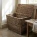 Open wicker laundry basket beside a rustic wooden bench with folded linens on it in a sunlit corner of a room.