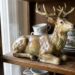 Ceramic deer figurine on a wooden shelf with porcelain teacups and plates in the background.