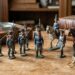 Row of blue-coated toy soldiers with rifles on a wooden desk, beside old books and a compass.”