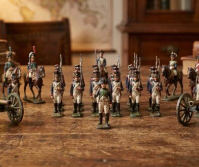 Miniature military figures arranged in rows with two small cannons on a wooden table, as if a tabletop display