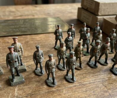 Assorted Elastolin toy soldiers lined up on a wooden table with boxes in the background.