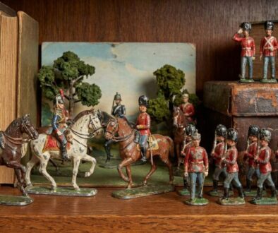 Vintage toy soldiers and cavalry figures arranged on a wooden shelf with antique books in the background.
