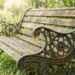 Weathered wooden park bench with ornate wrought-iron sides in a green garden setting.