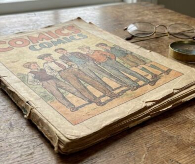 Old, creased comic book titled 'Comics' on a wooden table, with glasses and a magnifying glass nearby.