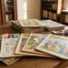 Pile of old children's magazines spread on a wooden table in a library, with a glove and magnifier nearby.