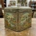 Decorative metal tin with oriental landscape panels and floral borders, square with a lid (vintage Asian-inspired design).