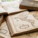 Open antique atlas and weathered books spread on a wooden table, with a magnifying glass nearby.