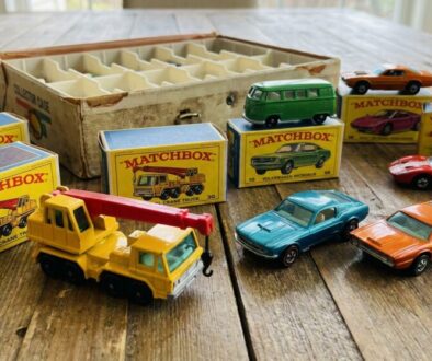 Assorted vintage Matchbox toy cars and a yellow crane truck on a wooden table with boxed sets in the background.