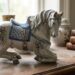 Ceramic horse figurine with blue patterned saddle on a wooden table beside vintage jars and old books.
