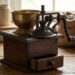 Vintage manual coffee grinder on a wooden table with a brass cup and burlap coffee beans in the background