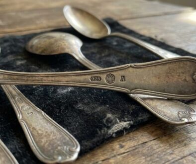 Old tarnished silver spoons resting on a dark cloth on a rustic wooden table, displaying 925 hallmarks.